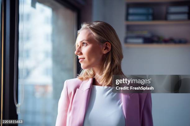 professional woman in bright office setting looking out of window - blouse stockfoto's en -beelden