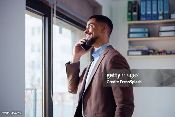 smiling businessman making a phone call in a bright office setting - boa postura imagens e fotografias de stock