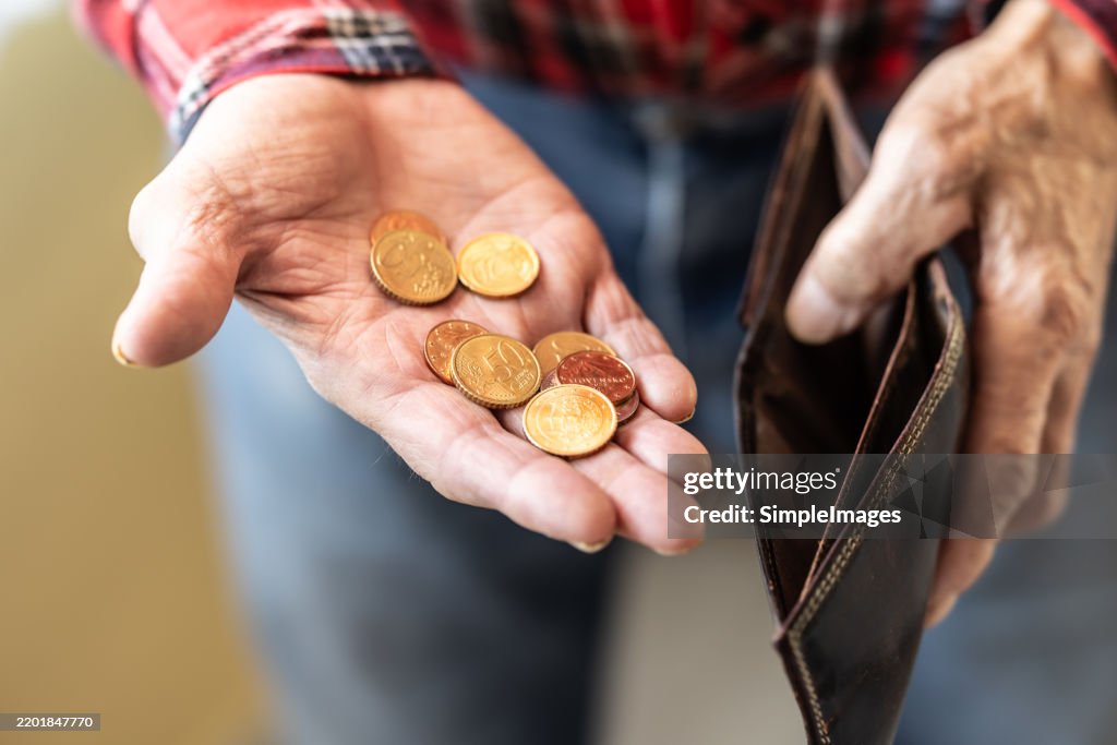 An old pensioner's hand holds an empty wallet and in the other hand he has a few coins