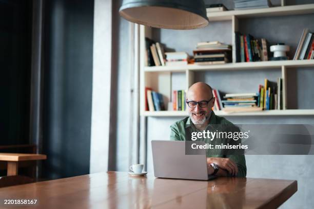 smiling man working on laptop in modern workspace with bookshelves - notebook imagens e fotografias de stock