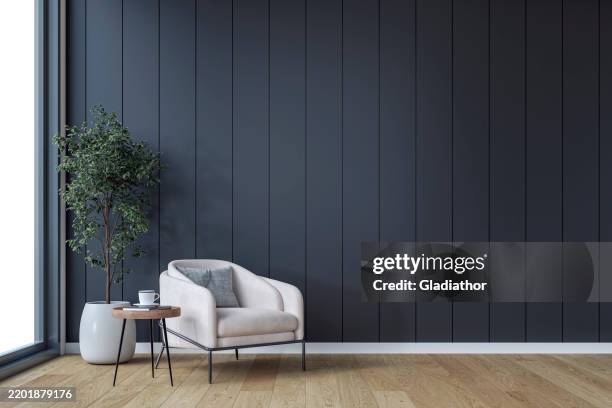 ein minimalistisches, unmöbliertes interieur mit einem gemütlichen sessel, einem beistelltisch und einer topfpflanze vor einem leeren, schwarz getäfelten akzentwandhintergrund mit kopierraum und einem fenster - einfaches leben stock-fotos und bilder