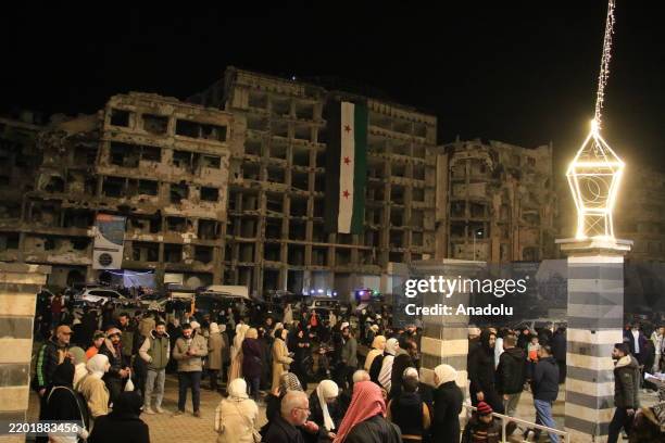 Citizens are seen in front of damaged buildings as Muslims gather at the Khalid ibn al-Walid Mosque to perform the first tarawih prayer of the holy...