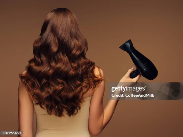 frau stylt langes, gewelltes haar mit einem professionellen haartrockner - haare föhnen stock-fotos und bilder