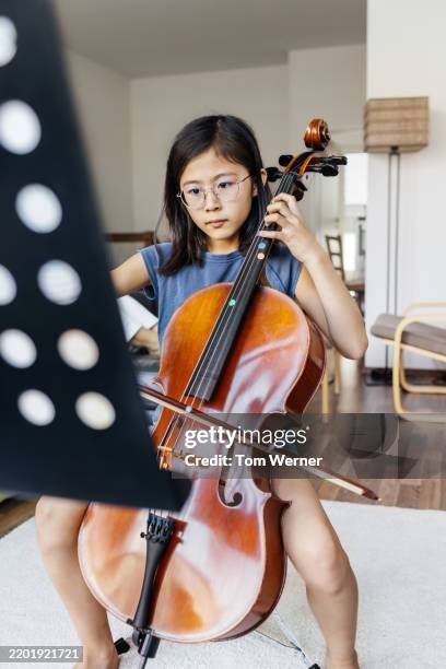 young girl practicing the cello while reading sheet music - classical musician stock pictures, royalty-free photos & images