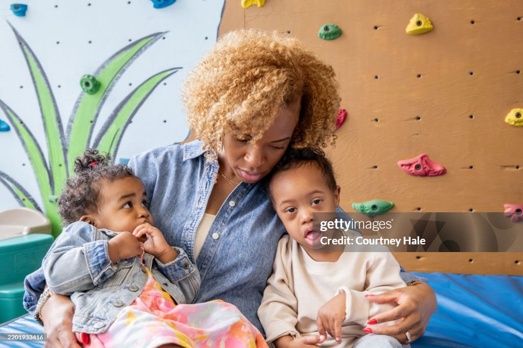 Mother comforts her toddler daughter and preschool age son who has Down Syndrome