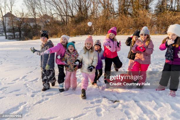 large group of elementary age kids throw snowballs while playing outside on snowy day - ski-wear stock pictures, royalty-free photos & images