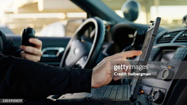 cop sitting in parked police car using laptop and radio - politieauto stockfoto's en -beelden