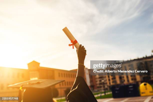 young black student holds up graduation diploma at sunset - akademischer grad stock-fotos und bilder