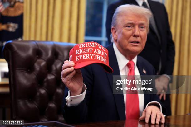 President Donald Trump holds up a hat stating "Trump Was Right About Everything" after signing executive orders in the Oval Office at the White House...