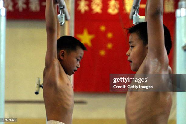 Two male students struggle to keep themselves suspended on the parallel bars at the state owned Shichahai sports school July 25, 2003 in Beijing,...