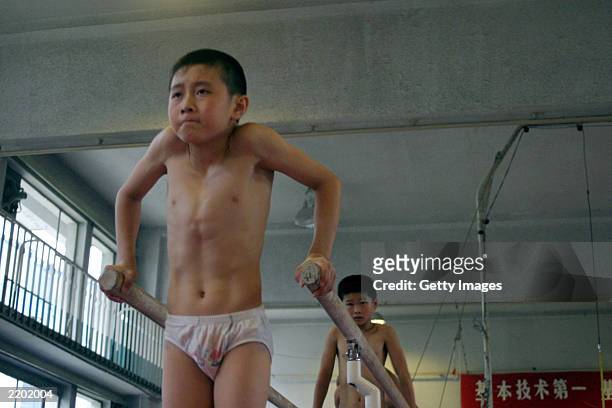 Young student attempts to keep himself upright on the parallel bars at the state owned Shichahai sports school July 25, 2003 in Beijing, China. The...