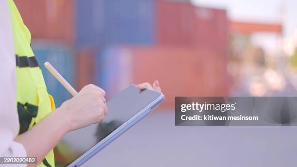 close up. hand of female engineer or technician or worker wearing safety vest, standing to work in loading container yard to checklist cargo container and control loading of cargo and container truck according to the transport plan in applications on tabl - dock worker stock pictures, royalty-free photos & images