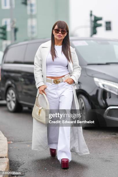 Elena Kruchenska wears burgundy bordeaux sunglasses, gold chain necklace with white floral detail, white t-shirt, cream trench coat, cream Gucci...