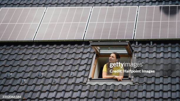 beautiful woman looking out of a skylight with a rooftop solar panel system above her. - solpanel bildbanksfoton och bilder