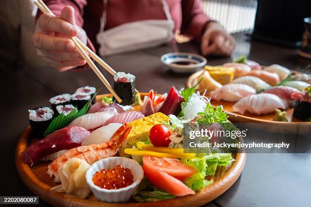 close-up of people eating freshly prepared sushi with side dishes and green tea at a japanese restaurant. - japanese food stock pictures, royalty-free photos & images