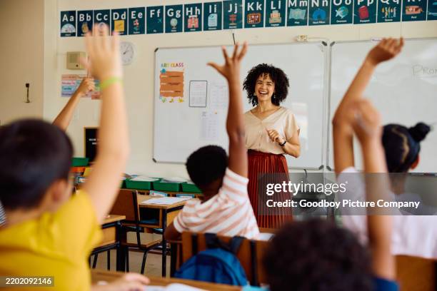 grundschullehrer lächelt und stellt fragen, kinder mit erhobenen händen - lehrkraft stock-fotos und bilder