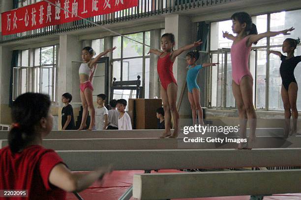 Female gymnasts train on balancing beams under supervision from their teacher at the state owned Shichahai sports school July 25, 2003 in Beijing,...