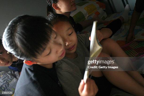 Student reads a book to a young girl during a break at noon in the dormitory of the state owned Shichahai sports school July 25, 2003 in Beijing,...