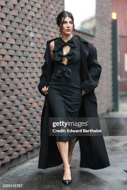 Giulia Salemi wears silver hoop earrings, black bow cutout sleeveless N21 midi dress, black trench coat, shiny black pointed toe mule heels leather...