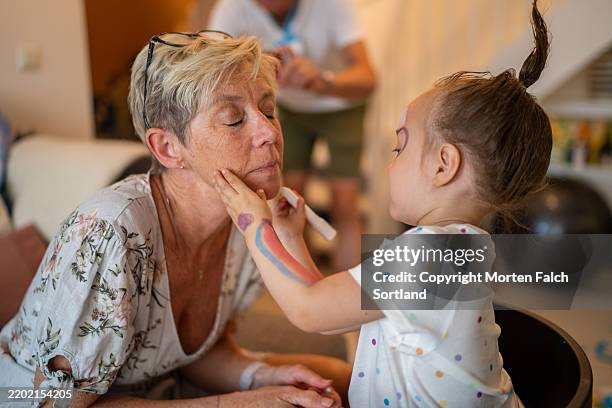 a mixed-race grandchild is drawing on her grandmother's face. - kort haar stockfoto's en -beelden