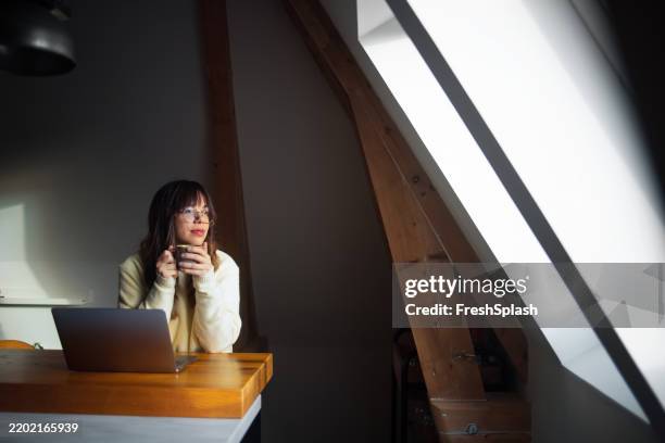 woman working remotely while enjoying coffee in a bright modern space - attic stock pictures, royalty-free photos & images
