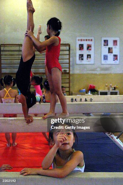 Young gymnast points upward while her fellow students exercise on a balance beam at the state owned Shichahai sports school July 25, 2003 in Beijing,...