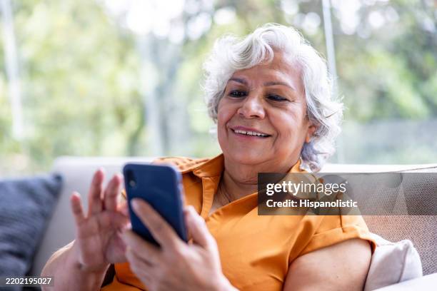 mujer mayor enviando mensajes de texto en su teléfono celular y sonriendo - una sola mujer mayor fotografías e imágenes de stock