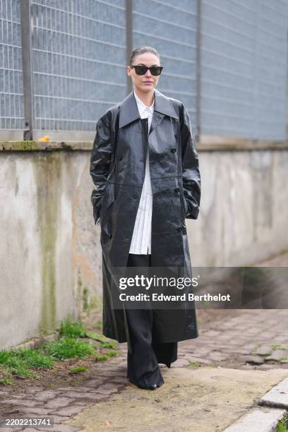 Sofia Roe wears black sunglasses, white buttoned up long sleeve oversized shirt, black baggy loose trouser pants, shiny black double breasted leather...