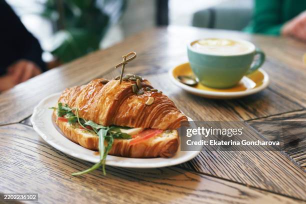 freshly prepared croissant sandwich and cappuccino on a wooden cafe table - comida salada fotografías e imágenes de stock