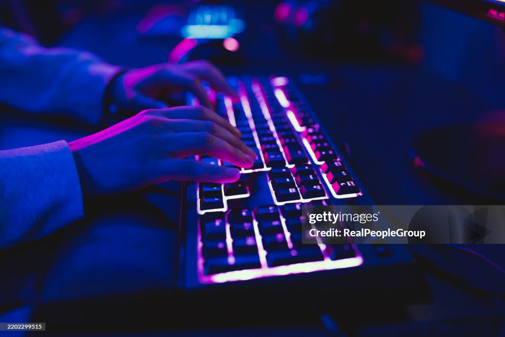 Gamer playing videogame on a backlit keyboard in a dark room