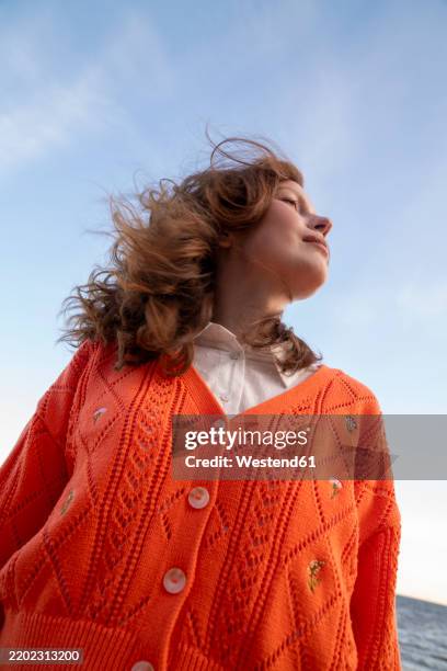 young woman wearing orange sweater standing under sky - una sola mujer joven fotografías e imágenes de stock
