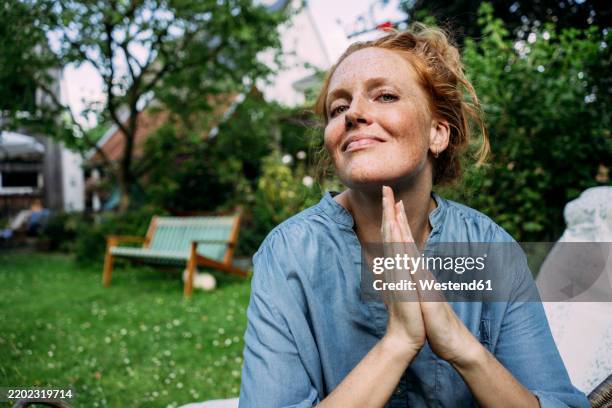 smiling redhead woman with hands clasped in back yard - dankbarkeit stock-fotos und bilder