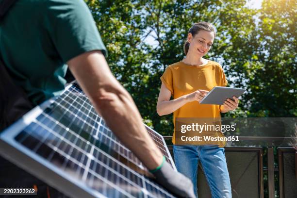 woman using tablet pc by engineer holding solar panel - solar equipment stock pictures, royalty-free photos & images