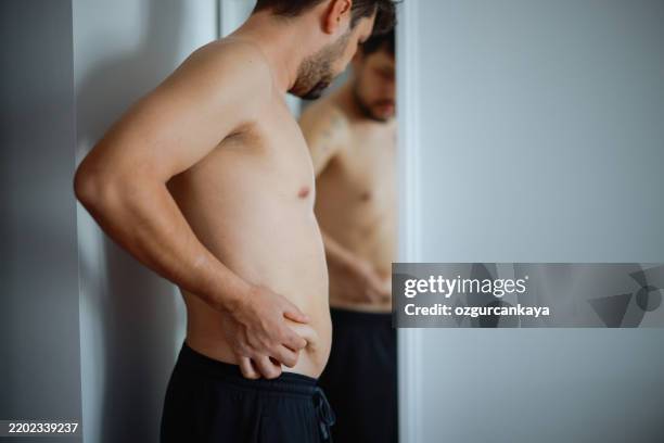overweight man checking his fat body reflection in mirror - cellulite stock pictures, royalty-free photos & images