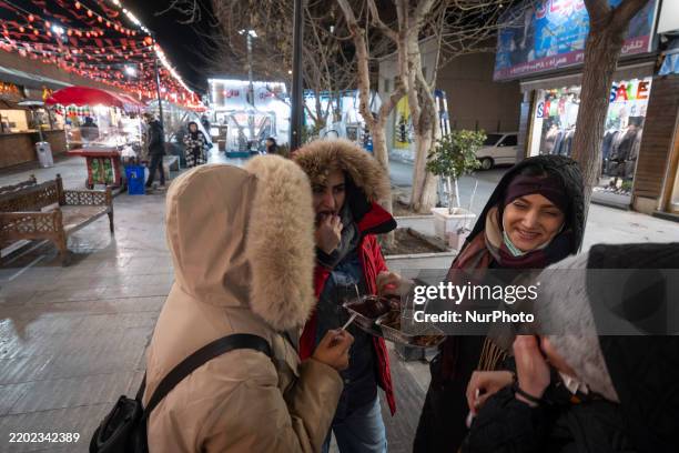 Young Iranian women eat beans while standing together on the street at the end of the first day of the holy month of Ramadan in southern Tehran,...