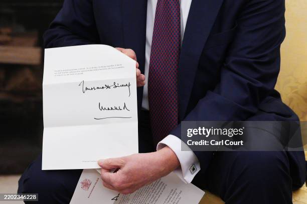 President Donald Trump shows an invitation from King Charles III for a second state visit during a meeting with UK Prime Minister Keir Starmer at the...