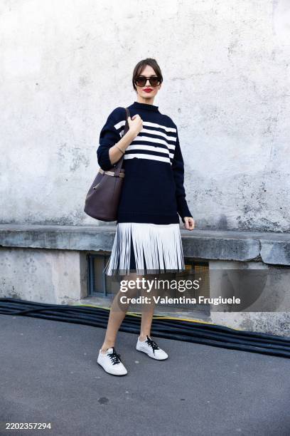 Gabrielle Caunesil Pozzoli wears black sunglasses, a white fringes skirt, white and blue snakers, a blue and white striped sweater and a bordeaux...