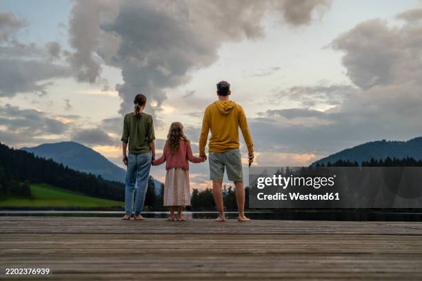 girl holding hands of mother and father on jetty in evening - ponton photos et images de collection