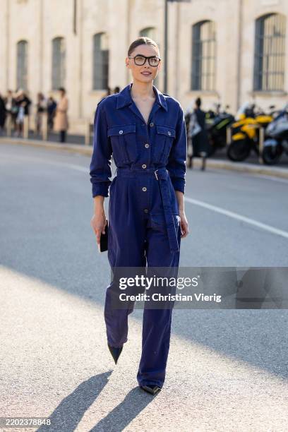 Bambi Northwood Blyth wears navy blue belted overall, glasses outside Prada during the Milan Fashion Week Womenswear Fall/Winter 2025/2026 on...
