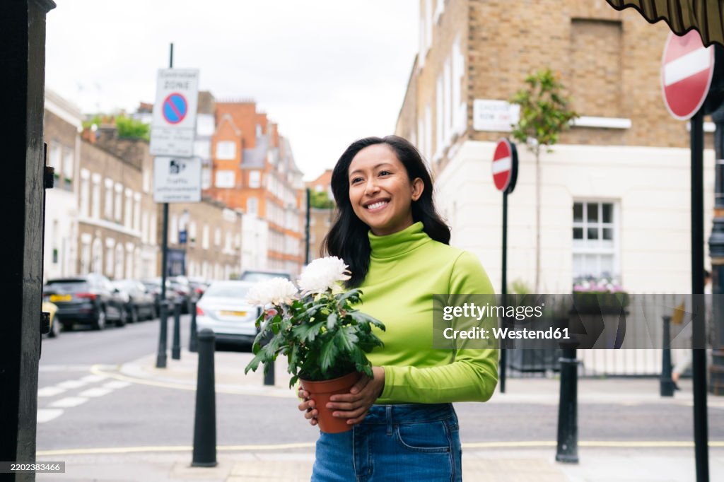 Happy woman holding potted plant and standing on street