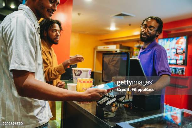 friends are buying popcorn and cola at the bar counter of the movie theatre - mobile payment stock pictures, royalty-free photos & images