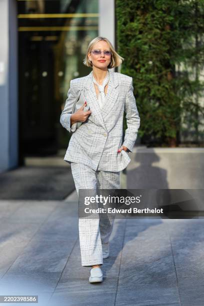 Violet Atkinson wears blonde bob hair, light purple sunglasses, silver earrings, light gray pattern necktie, light gray plaid pattern double breasted...