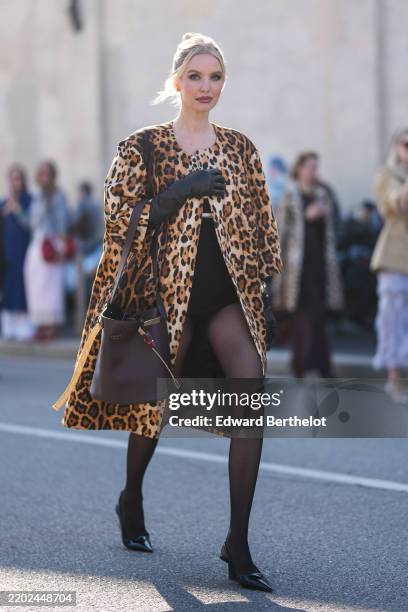 Leonie Hanne wears black sunglasses, light brown leopard pattern/print Prada cape, shiny black Prada leather gloves, gold bracelet, dark gray sheer...
