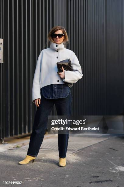 Guest wears black sunglasses, cream high neck coat, shiny deep dark brown woven leather handbag, dark navy blue straight denim jean pants, light pale...