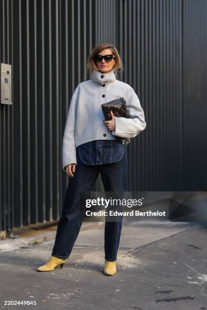 Guest wears black sunglasses, cream high neck coat, shiny deep dark brown woven leather handbag, dark navy blue straight denim jean pants, light pale...