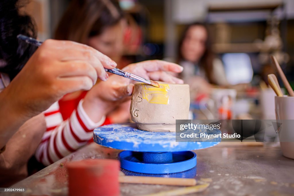 A young woman carefully paints a small clay cup during a pottery class