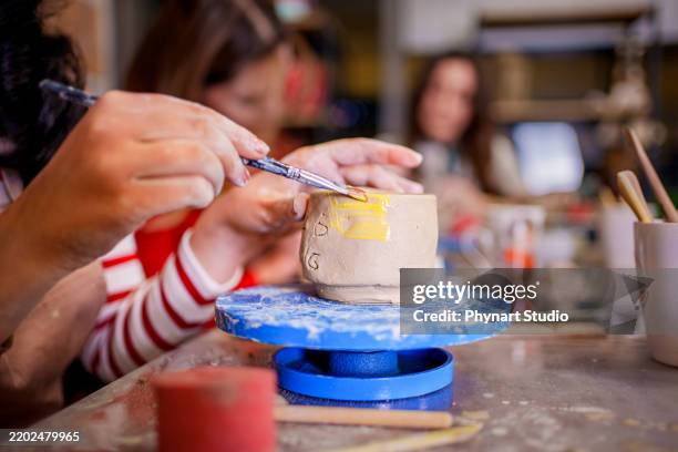 a young woman carefully paints a small clay cup during a pottery class - clay painting stock pictures, royalty-free photos & images