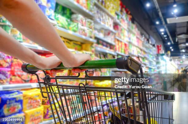 a woman pushes a shopping cart to choose products in a supermarket. - rollwagen stock-fotos und bilder
