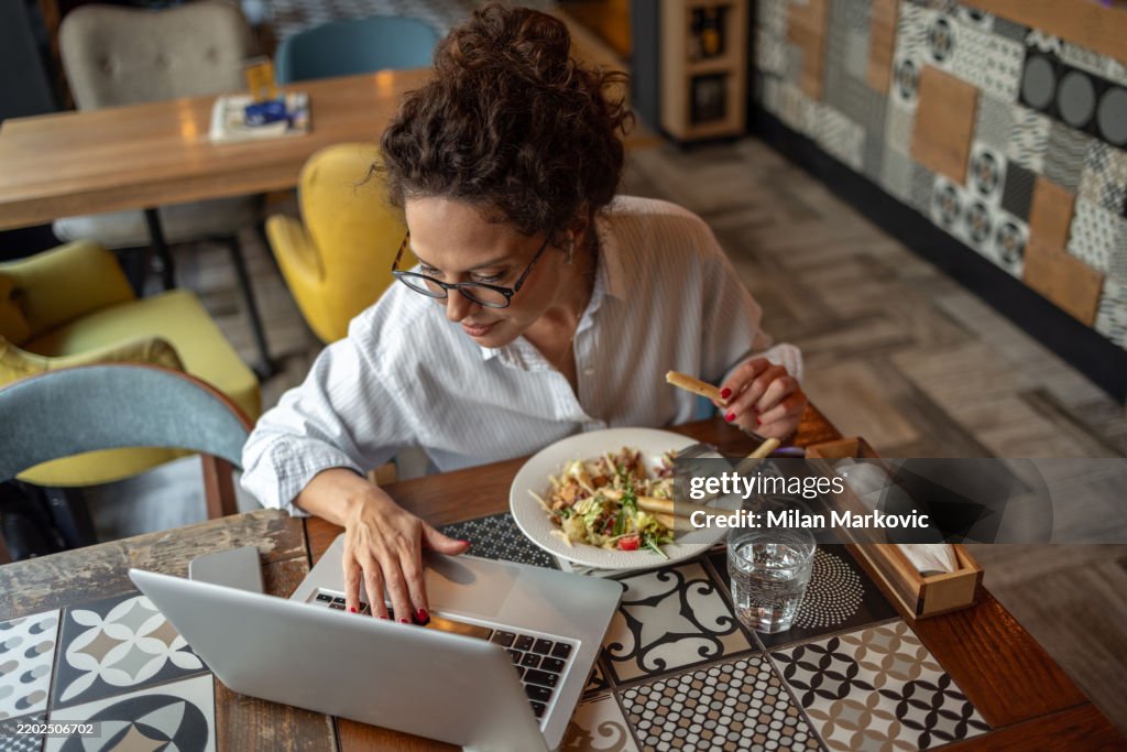 Freiberufler, der am Laptop arbeitet und Salat im Restaurant isst