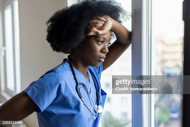 female doctor in despair looking through window - tired healthcare worker stock pictures, royalty-free photos & images